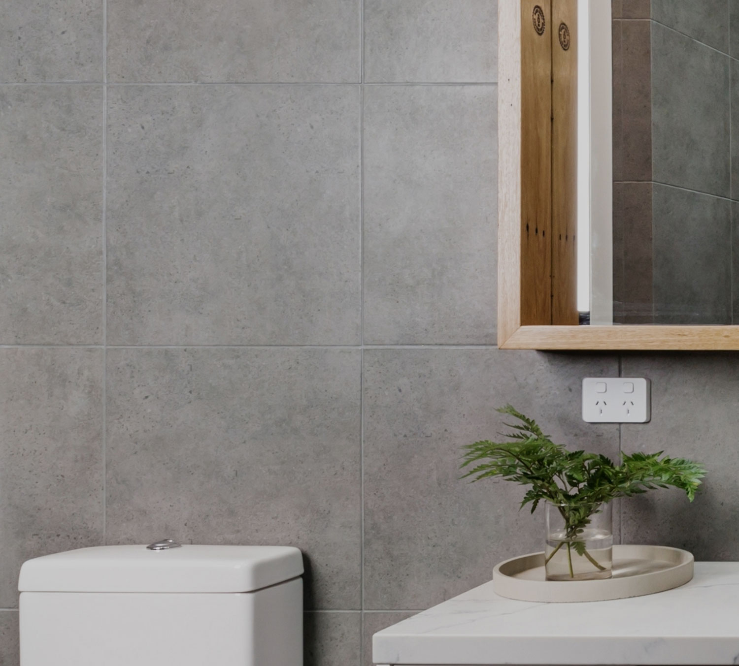 Compact New Zealand bathroom with grey tiling, a timber framed mirror and a wall mounted vanity